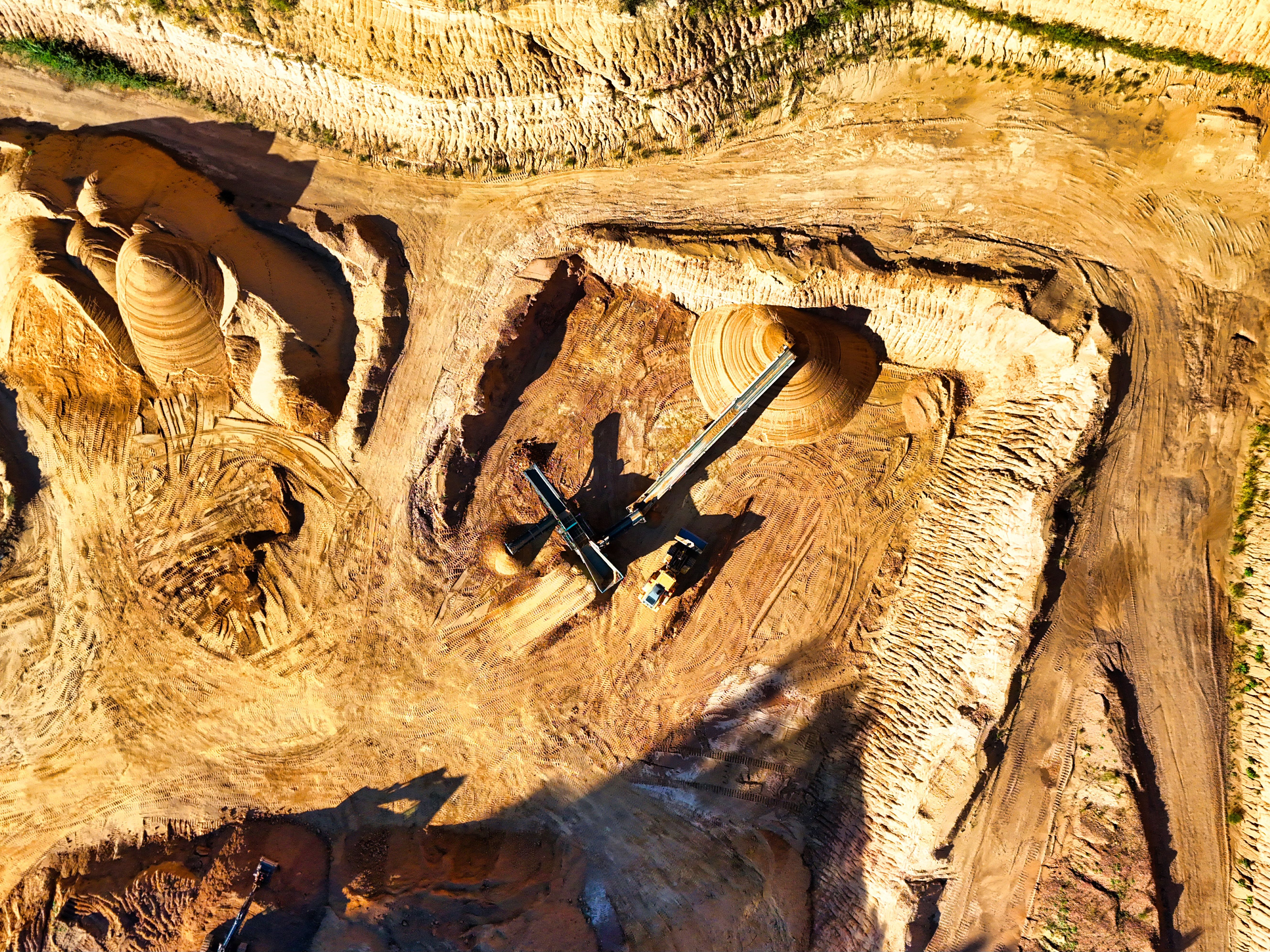 An aerial view of an open-pit mine, where heavy machinery excavates raw materials from the earth.